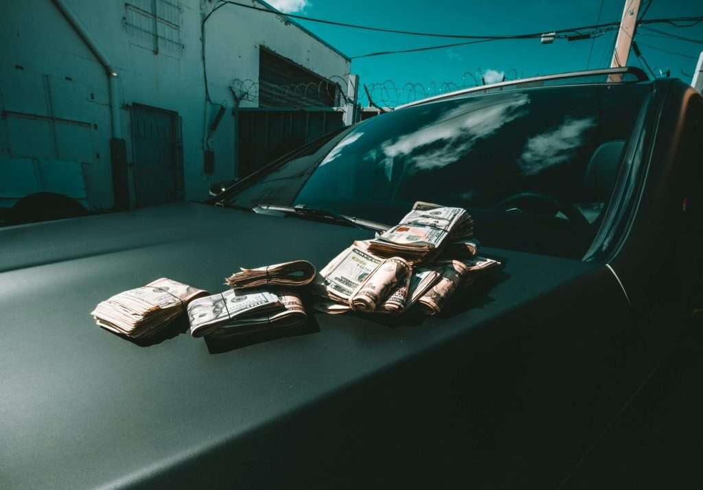 Stacks of cash on a car hood at Ideal Auto Bensonhurst, pre owned car Brooklyn.